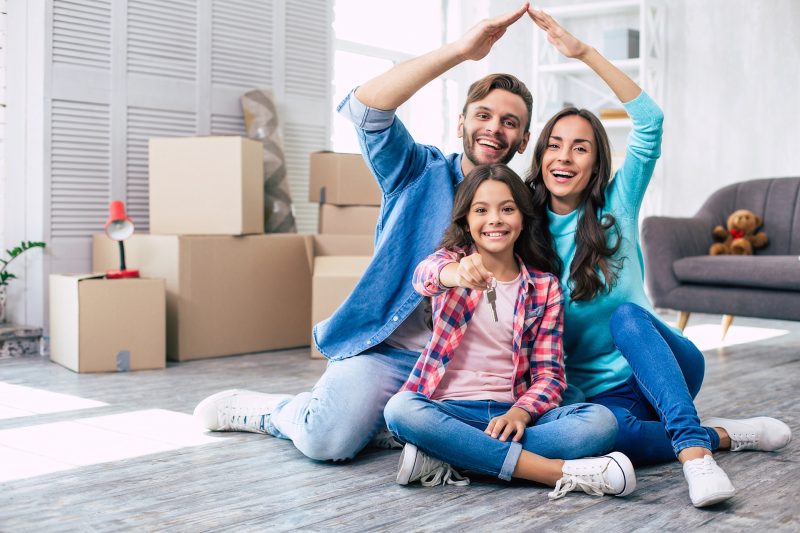 Mom and dad are imitating a roof of the house with their hands while their daughter holds keys from their new apartment in her hands. House moving concept